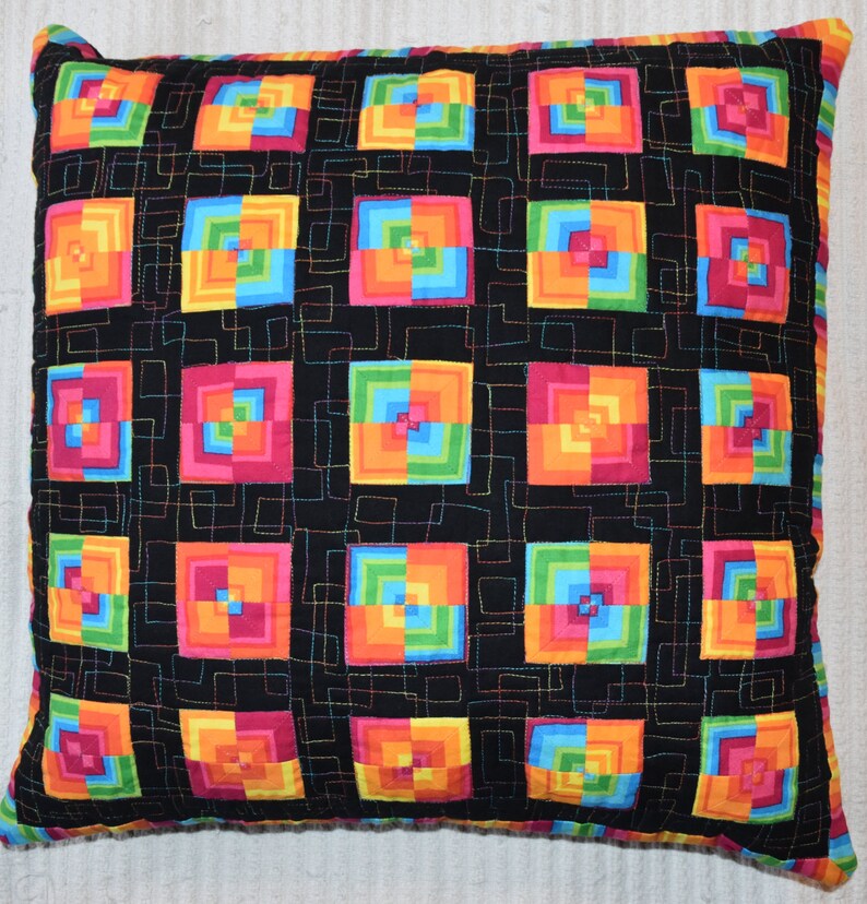 May include: A black pillow with a colorful geometric pattern of squares within squares. The squares are in shades of orange, yellow, green, blue, pink, and red.