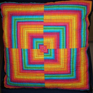 May include: A colorful pillow with a geometric pattern of concentric squares in shades of red, orange, yellow, green, blue, and pink.