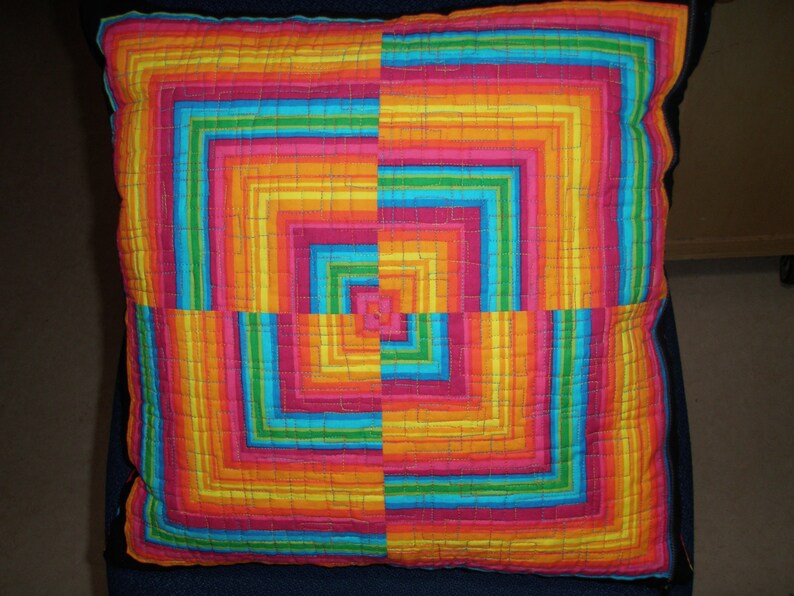 May include: A colorful pillow with a geometric pattern of concentric squares in shades of red, orange, yellow, green, blue, and pink.