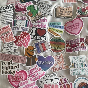 May include: A collection of colorful stickers with book-related themes. The stickers feature phrases like "I read past my bedtime," "Read more books," and "Book Lover." Various designs include books, hearts, and a dinosaur reading.