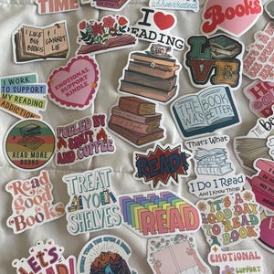 May include: A collection of colorful stickers with book-themed designs and text. The stickers feature phrases like "Read Good Books," "Books Because Reality is Overrated," and "I Love Reading." Various illustrations of books and related imagery are also included.