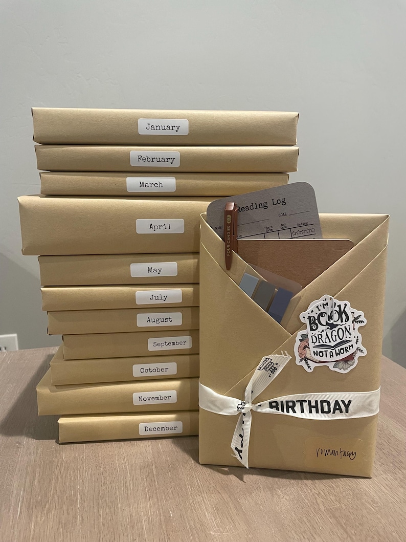 May include: A stack of twelve brown wrapped books with labels for each month of the year. The top book is wrapped in brown paper with a white ribbon and a sticker that says "I'm a book dragon, not a worm". The book is labeled "Birthday" and "romantasy".
