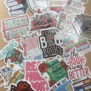 May include: A collection of colorful stickers with book-themed designs. The stickers feature phrases like "Never Enough Books," "Book Nerd," and "I Like Books." Various designs include stacks of books, open books with floral arrangements, and a cat sleeping on books.