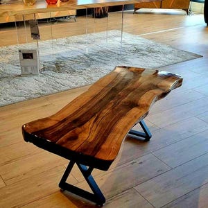 Peut inclure: Une table basse à bordure vive avec un fini de grain de bois foncé. La table est soutenue par des pieds en métal noir en forme de X. Le dessus de la table a une forme naturelle et organique.