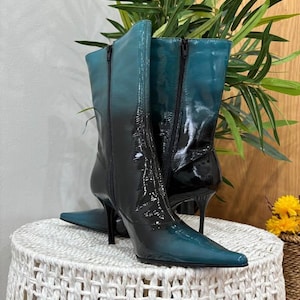 Peut inclure: Une paire de bottes mi-mollet avec une finition vernie brillante présentant un dégradé de couleur passant du bleu sarcelle profond en haut au noir uni à la base. Les bottes ont un bout pointu, un talon aiguille fin et une fermeture éclair latérale.