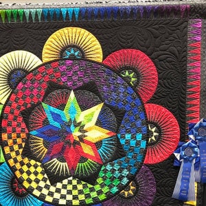 Pode incluir: Um cobertor colorido com um design de estrela no centro. O cobertor é feito de tecido preto com uma variedade de cores, incluindo vermelho, laranja, amarelo, verde, azul e roxo. O cobertor é enfeitado com uma borda colorida do arco-íris.