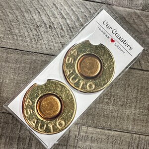 May include: Two round car coasters with a 45 AUTO design. The coasters are made of a cork-like material and have a brown and gold color scheme.