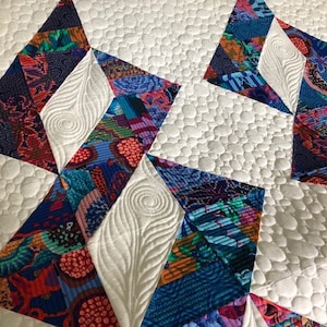 May include: A white quilt with a geometric pattern of colorful fabric squares. The quilt is quilted with a pebble stitch pattern.