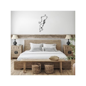 May include: A black metal wall art piece in the shape of a coastline, mounted above a wooden bed frame. The bedroom features a light-colored wooden bed, nightstands, and a bench. Two wicker baskets sit at the foot of the bed.