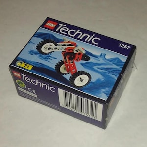 Op de afbeelding: Een doos LEGO Technic set met een rood en wit motorfietsmodel. De doos heeft een blauwe achtergrond met het woord "Technic" en het nummer "1257". De set is voor kinderen vanaf 7 jaar.