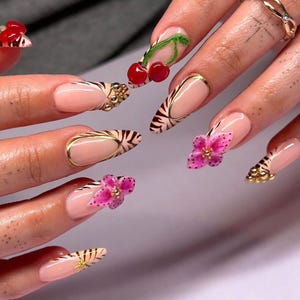 May include: Close-up of several long, almond-shaped nails with a zebra print design. Some nails are accented with a gold stripe, a pink flower, or a red cherry.