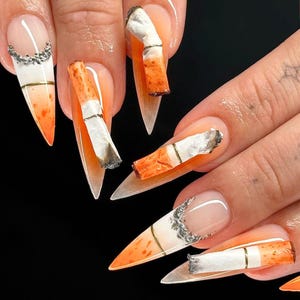 May include: Close-up of several long, pointed fingernails with orange and white nail polish. Each nail is decorated with a miniature cigarette, some with the filter end visible.