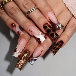 May include: Long, stiletto-shaped nails with a variety of designs. Some nails are painted with a white and brown swirl pattern, while others feature a brown and black tortoiseshell pattern. Some nails have gold accents.