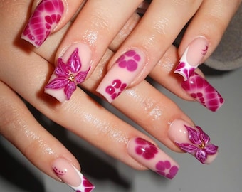 May include: Pink and white nail art with floral designs. The nails are long and have a French manicure style with white tips. Some nails have 3D flowers.