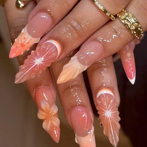 Puede incluir: Primer plano de una mano con uñas largas, rosas y blancas decoradas con diseños en 3D de flores y cítricos.