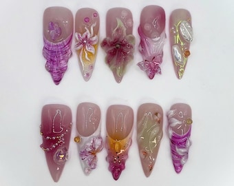 May include: Ten pink and white artificial nails with intricate floral and butterfly designs. The nails are decorated with 3D flowers, glitter, and pearls.
