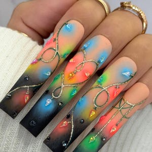 May include: Long, almond-shaped nails with a gradient ombre design featuring a black to rainbow colour transition. The nails are decorated with a string of colourful lights and gold glitter.