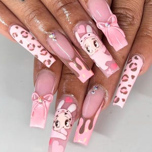 May include: Pink and brown long, almond-shaped nails with various designs. Some nails have a pink and brown leopard print, some have a pink and brown drip design, some have a pink bow, and some have a cartoon bunny with a pink heart.