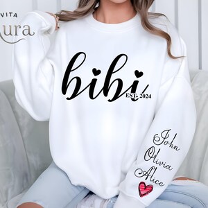 May include: White sweatshirt with the text "bihi" in black cursive lettering with two small hearts above the text and "EST. 2024" below. The sweatshirt has the names "John", "Olivia", and "Alice" written on the sleeve with a red heart.
