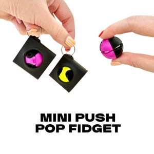 Può includere: Due giocattoli fidget quadrati neri con elementi push pop rosa e gialli, tenuti in mano. Un giocattolo fidget a forma di palla nera e rosa è tenuto in un'altra mano. Il testo "MINI PUSH POP FIDGET" è visualizzato in grassetto, con lettere nere.