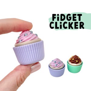 Könnte beinhalten: Drei farbenfrohe Cupcake-förmige Fidget-Clicker. Die Clicker sind lila, grün und rosa mit weißem Frosting und silbernen Streuseln. Der Text "FIDGET CLICKER" ist in schwarzen Buchstaben auf grünem Hintergrund.