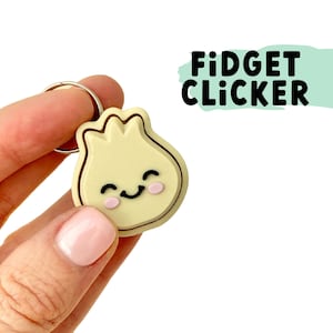 May include: A yellow, smiling, cartoon dumpling keychain with a silver ring. The keychain is labelled "Fidget Clicker".