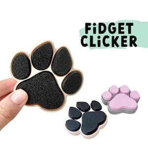 Può includere: Tre clic di fidget a forma di zampa in diversi colori. Il primo è beige con cuscinetti per zampe neri, il secondo è grigio con cuscinetti per zampe rosa e il terzo è beige con cuscinetti per zampe neri. Il testo "FIDGET CLICKER" è scritto in lettere nere su uno sfondo verde.