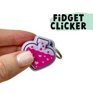 May include: A heart-shaped fidget clicker with a pink potion design and the text "Fidget Clicker". The clicker has a white border and a silver keyring.