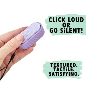 Pode incluir: Um pequeno brinquedo fidget lavanda com uma borda texturizada e canelada e um centro liso e circular. O texto "CLICK LOUD OR GO SILENT!" e "TEXTURED. TACTILE. SATISFYING." são exibidos na imagem.