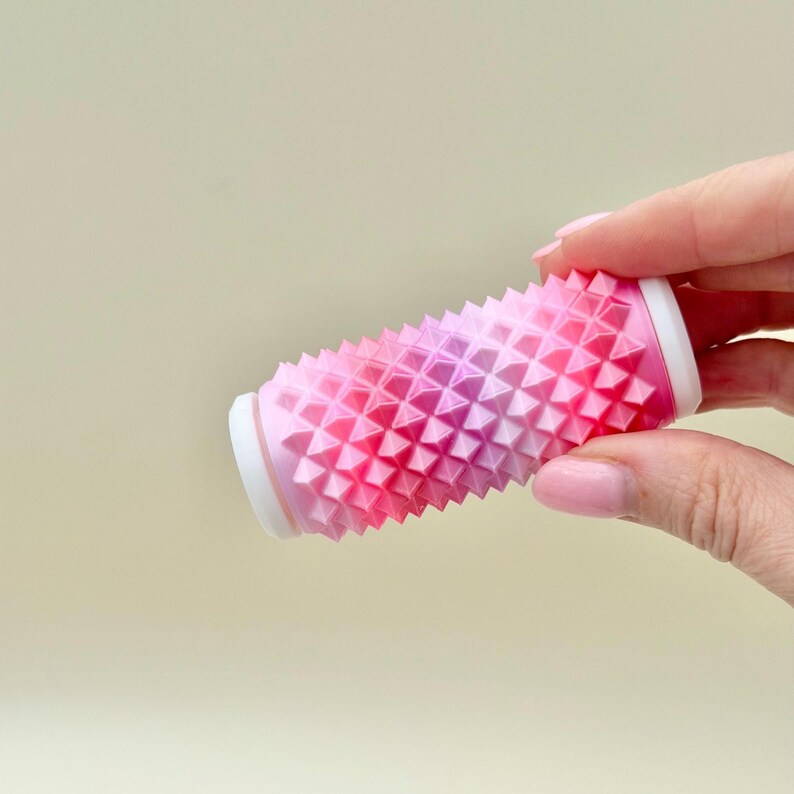 Hand holding pink gradient spiky roller, firm sensory fidget for stress and focus.