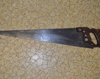 May include: A vintage hand saw with a dark, aged steel blade and a wooden handle. The handle is a dark brown color and is attached to the blade with metal rivets. The saw's teeth are clearly visible along the blade's edge.