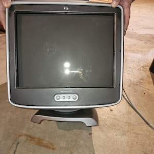 May include: A dark gray HP monitor with a silver base and trim. The screen is black, and the monitor has buttons on the bottom. The monitor is being held by a person.