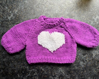 May include: A purple knitted sweater with a white heart design. The sweater has long sleeves and a crew neck.