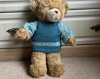 Può includere: Un orsacchiotto marrone che indossa un maglione di lana blu turchese con una striscia bianca.