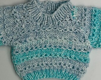 May include: A hand-knitted sweater featuring a variegated color pattern of light blue, sky blue, and bright turquoise. The garment has a ribbed crew neckline, long sleeves, and a textured stitch design with horizontal rows of yarn loops.
