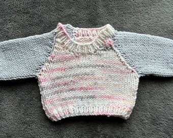 May include: A knitted baby sweater with a pink and white striped body and gray sleeves.
