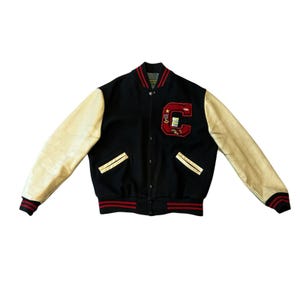 May include: A varsity jacket featuring a black wool-blend body and cream-colored sleeves. The front displays a large red letter C patch with small embroidered details, a snap-button closure, two side pockets, and red and black striped ribbed trim.
