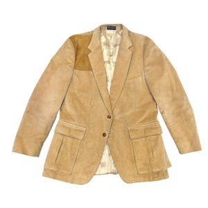 May include: Tan corduroy blazer with a suede shoulder patch. The jacket has two front pockets and a two-button closure. The interior lining is a patterned cream color.