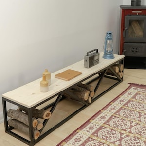 Könnte beinhalten: Ein Holz- und Schwarzmetall-Holzregal mit einer weißen Oberseite. Das Regal ist mit Holzscheiten gefüllt und hat ein Buch, zwei Flaschen und ein Radio darauf. Das Regal steht vor einem roten Holzofen.