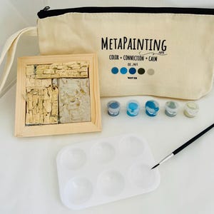 May include: A MetaPainting kit with a beige canvas bag, a wooden-framed mosaic, paint pots, a palette, and a paintbrush. The bag has the text "MetaPainting" and "Color + Connection + Calm". The mosaic is made of beige and gray stone.