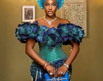 May include: A woman wearing a teal and blue sequined dress with a matching head wrap. She is holding a blue clutch with a bow.