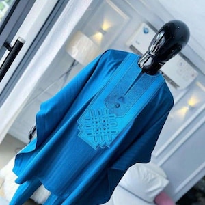 May include: A blue two-piece outfit on a mannequin. The top features detailed embroidery around the neckline and chest. The outfit is made of a flowing fabric, likely a traditional garment. The mannequin has a black head.
