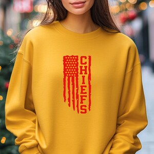 May include: A yellow sweatshirt featuring a red American flag design with the word "CHIEFS" printed vertically on the flag.