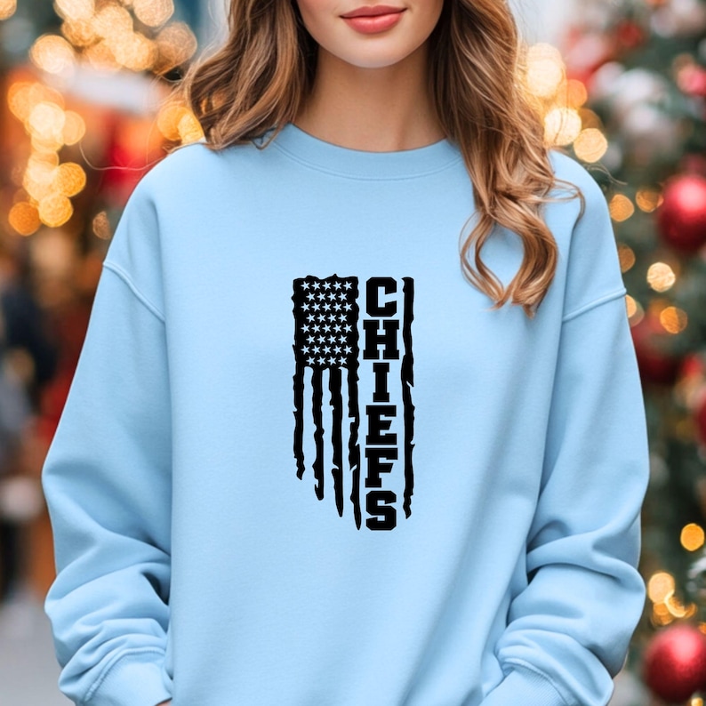 May include: A light blue sweatshirt featuring a black distressed American flag design with the word "CHIEFS" printed vertically.