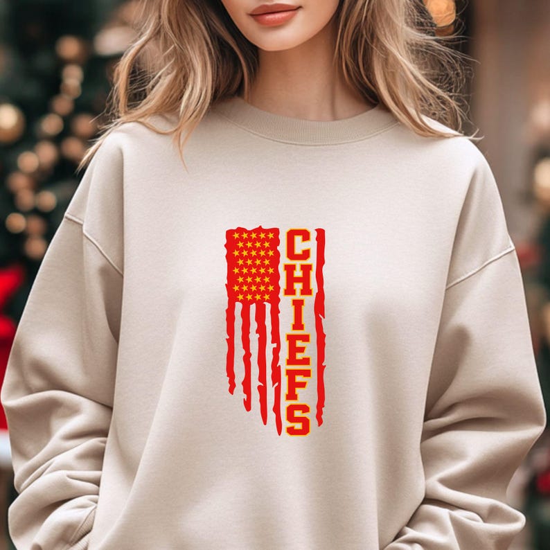 May include: A beige sweatshirt featuring a red and yellow American flag design with the word "CHIEFS" printed vertically on the right side of the flag.