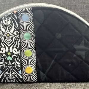 May include: A black quilted makeup bag with a zipper closure. The front of the bag features a colorful patterned fabric with a geometric design.