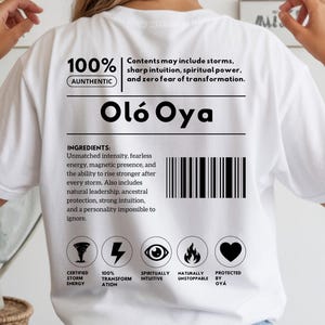 Puede incluir: Camiseta blanca con texto y gráficos negros. La camiseta presenta el texto "Oló Oya" y una lista de ingredientes. El texto adicional incluye "100% Auténtico" e iconos que representan la energía de la tormenta, la transformación, la intuición y la protección.