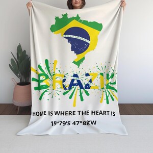 Puede incluir: Manta blanca con el mapa de Brasil en verde y amarillo, con los colores de la bandera brasileña. La palabra "BRAZIL" está en verde y amarillo, con el texto "HOME IS WHERE THE HEART IS" y coordenadas.