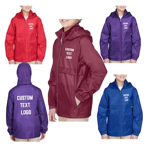 May include: A collection of hooded windbreakers in red, burgundy, purple, and blue. Each jacket has a front zipper, a pocket, and the text "CUSTOM TEXT LOGO" printed on the front or back. The jackets are designed for children.