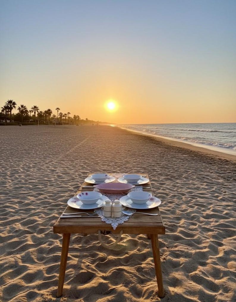 May include: A wooden table set for a meal on a sandy beach at sunset. The table holds plates, bowls, silverware, and salt and pepper shakers. The sun is setting over the ocean, with palm trees in the distance.
